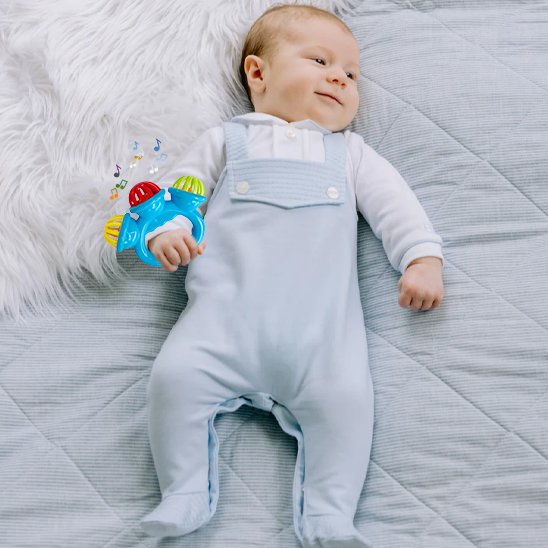 Bébé debout en salopette tenant un hochet bébé d’éveil