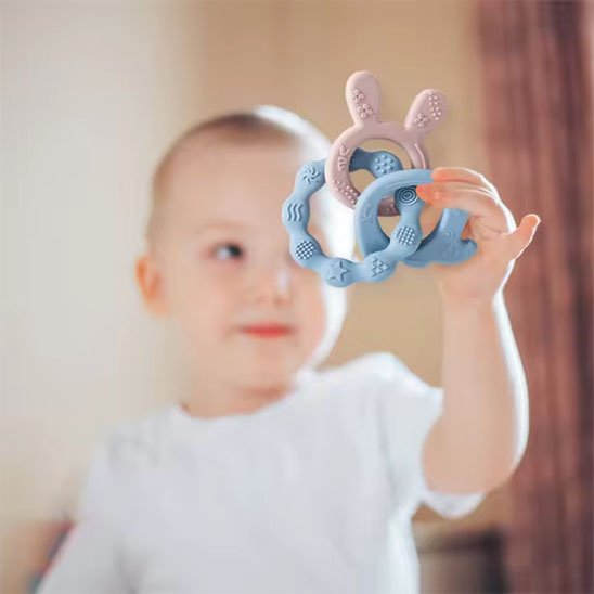 Bébé assis tenant un anneau de dentition en silicone bleu
