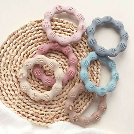 Lot d’anneaux de dentition en silicone pastel posés sur un panier en rotin